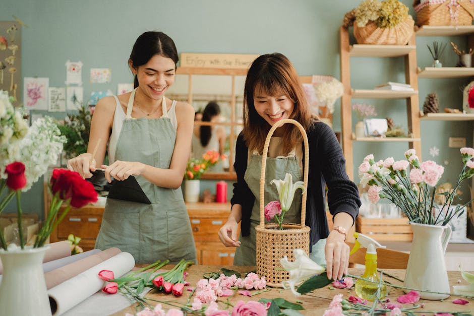 Two female florists happily arranging a floral bouquet in a cozy workshop.